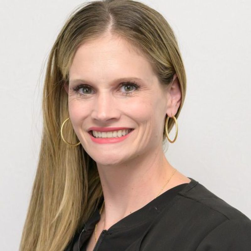 Dr. Leah Guempel, audiologist, smiling in a black top with gold hoop earrings